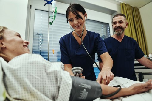 Foto einer Pflegefachkraft, die eine Patientin am Bett untersucht.