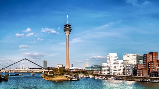 Bild von der Stadt Düsseldorf aus der Wasserperspektive. Mittig sind Brücken und ein Funkturm zu sehen.    